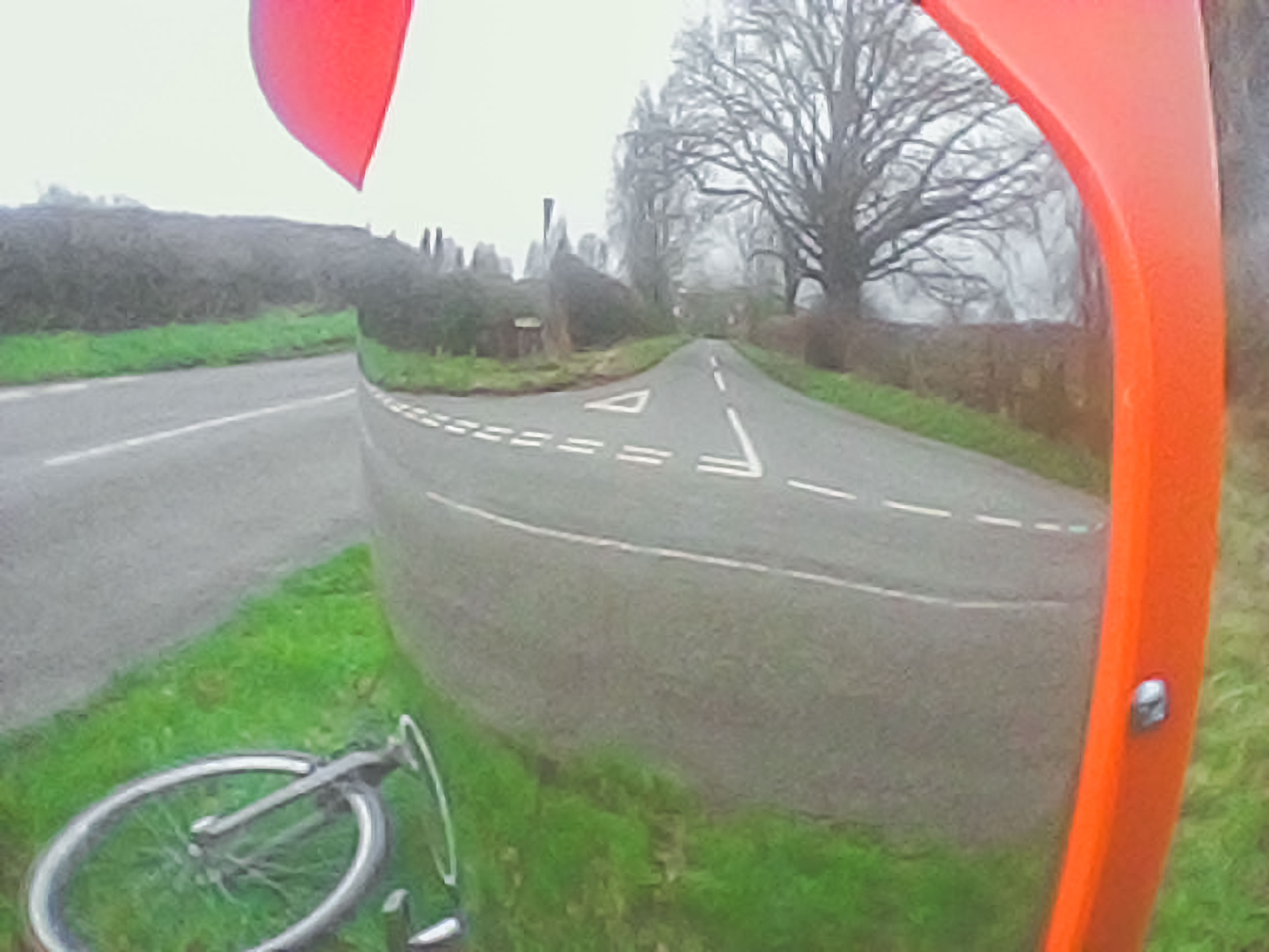 Shows a country road to the left, then the 180 degrees mirror with orange outside border, that is domed on the front, that then shows the road opposite that morphs the real road, and the reflection in the mirror.