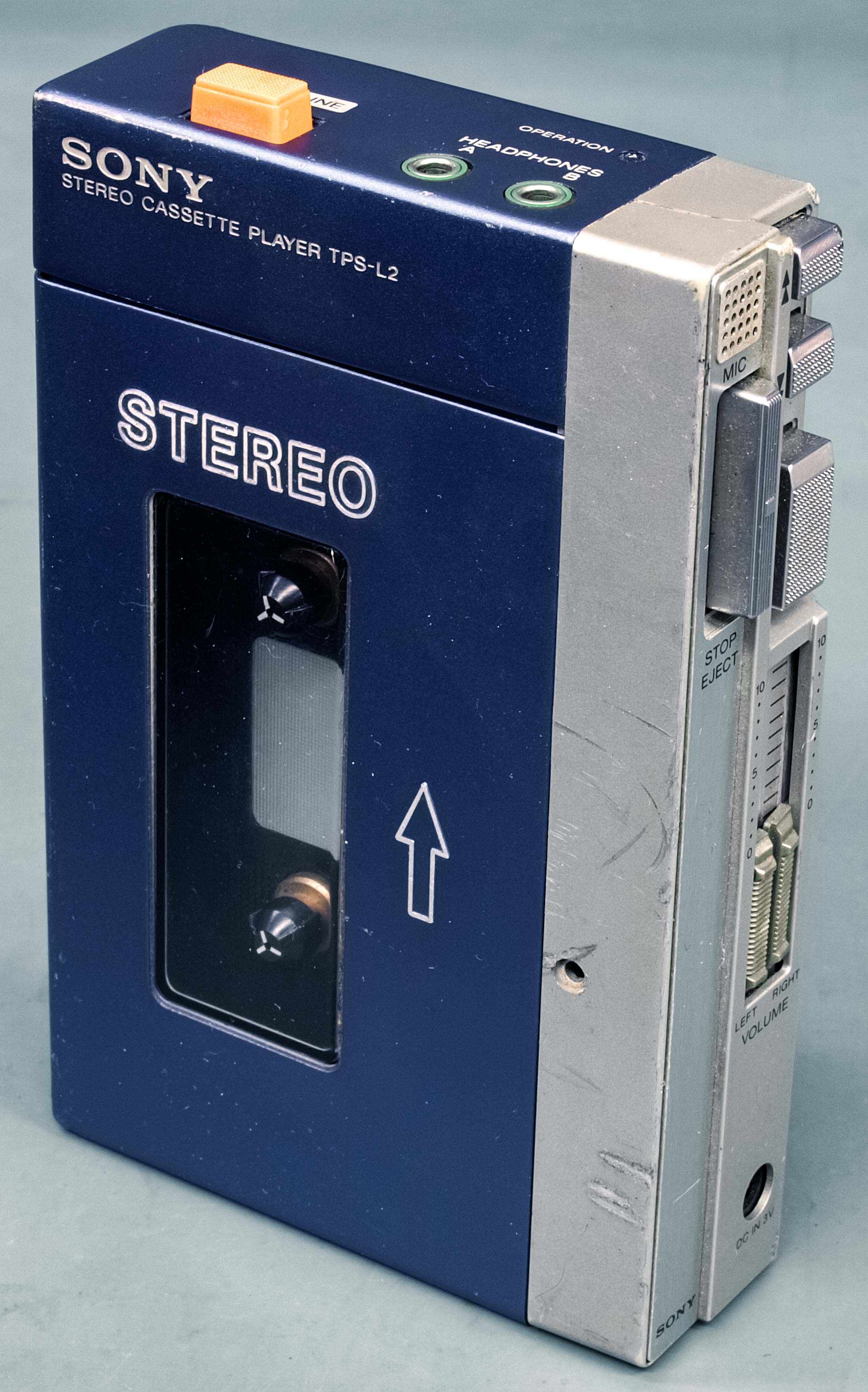 Side-on up-close photograph of the old cassette Walkman. Dark faded blue front, with steel side casing on the right, with steel buttons.