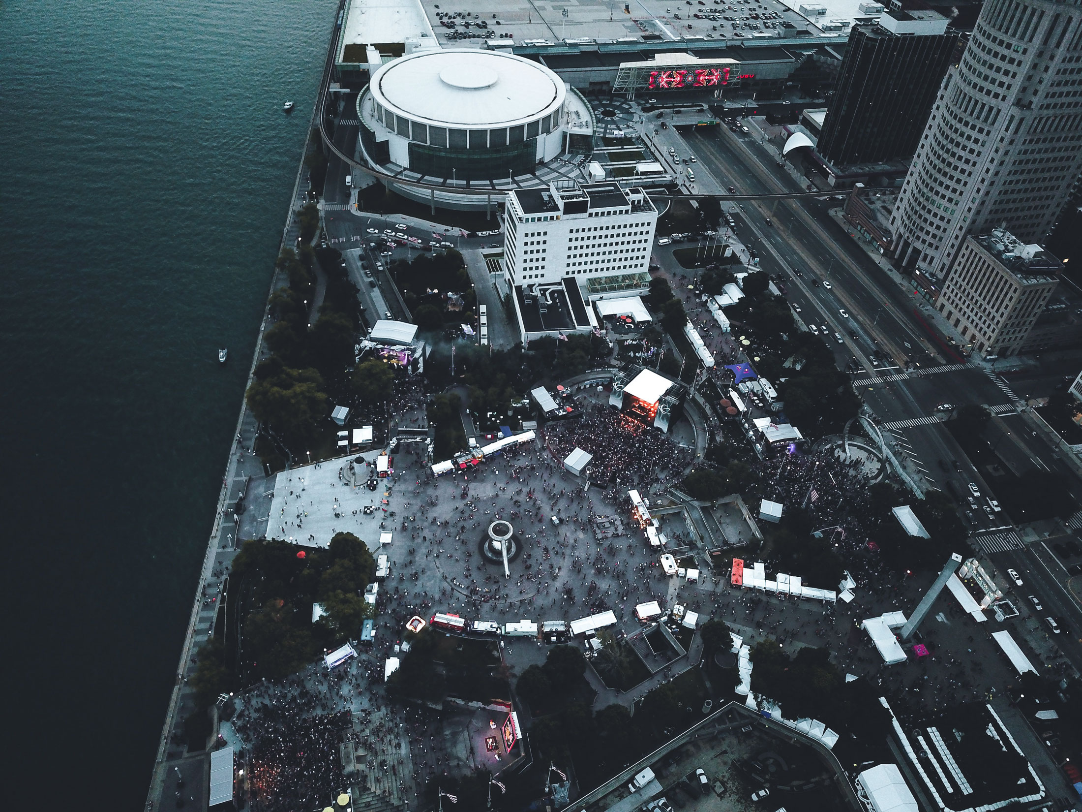 Aerial photo of Hart Plaza. Shows a crowd of people in front of the stage. Also shows the sea to the left, roads to the right, then tall skyscrapers on the right.