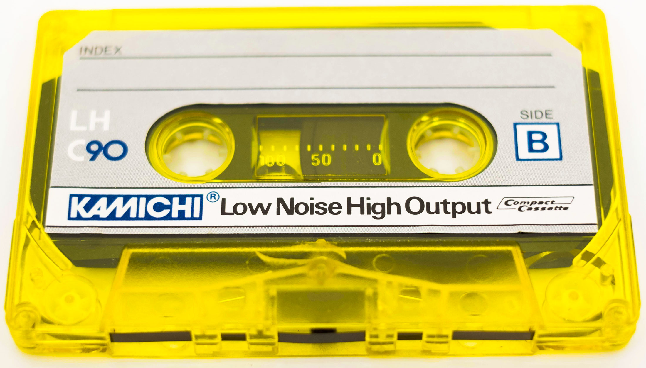 Close-up shot of a bright yellow tape cassette, shows the black tap inside, with a white branded sticker on the front, where you can write on it.
