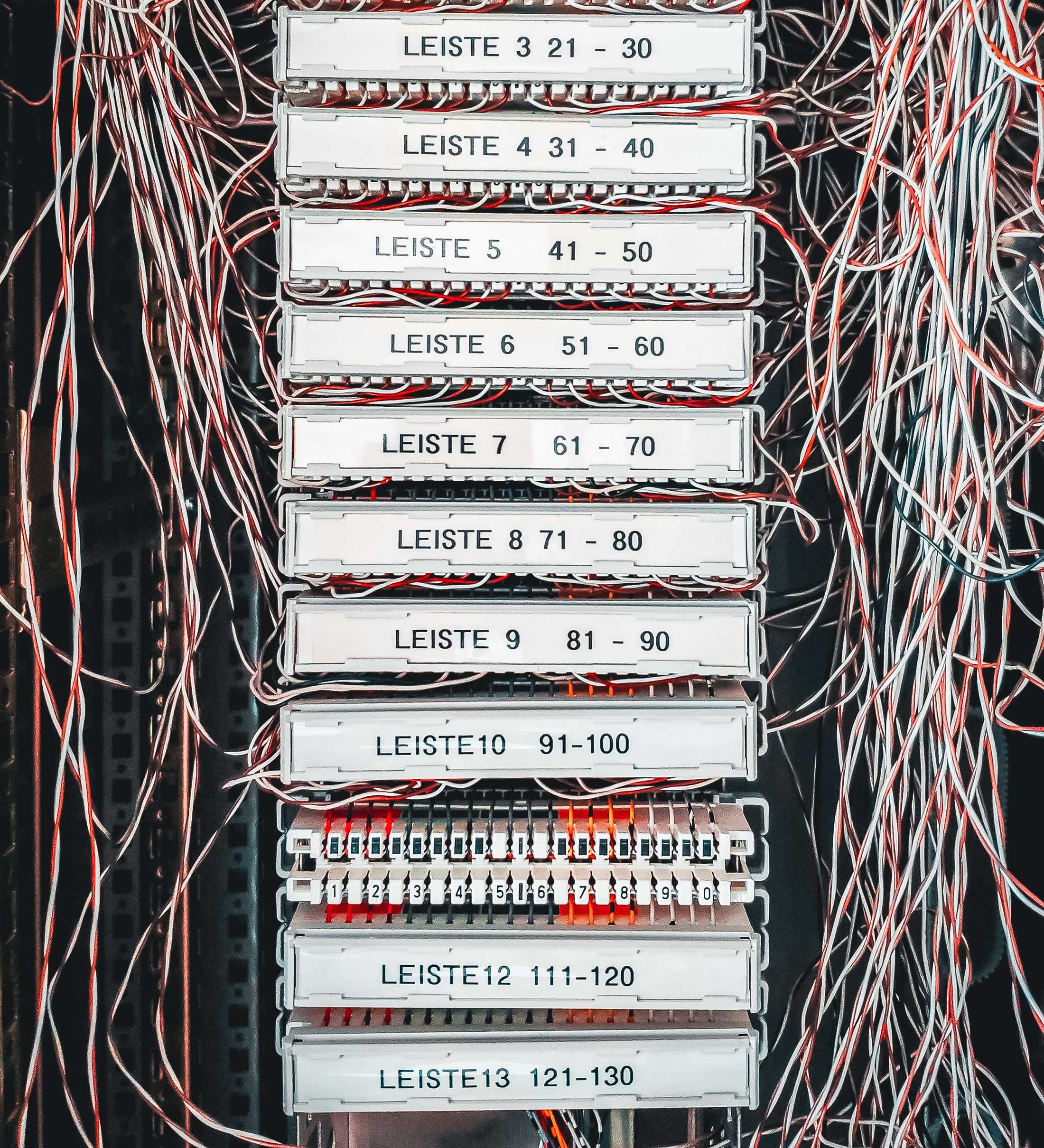 Front on photo or a vertical row of plastic name plates, with text behind them, then 1000s of small wires going into them and around them. Shows and old copper wire connector terminal.