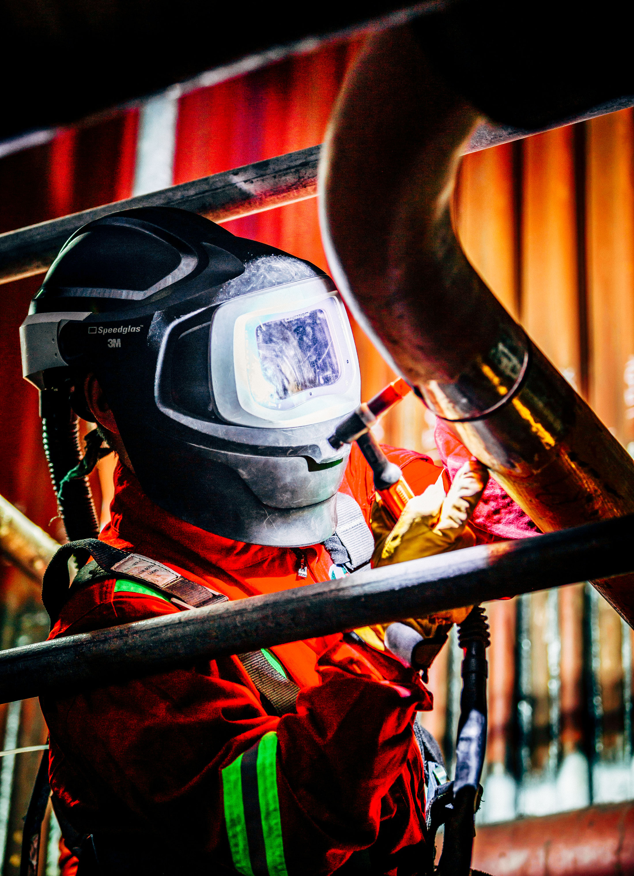 A technician welding person, fixing metal steel pipes. Wearing a safety hood and mask, set in an industrial factory.